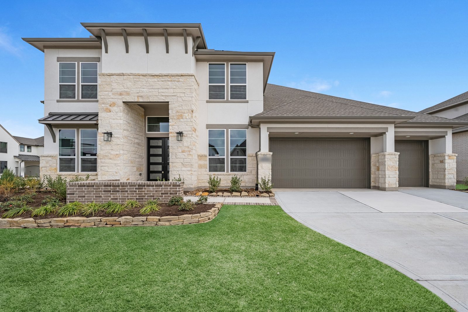 Two-story new-construction home with a cream stone entry tower, black glass front doors and a three-car garage