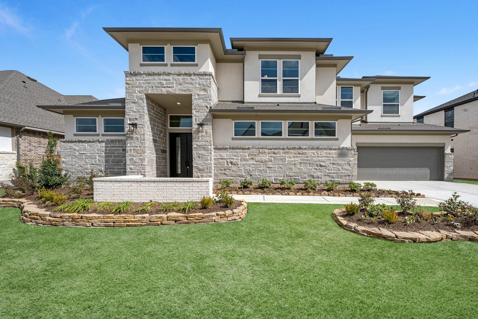 Two-story contemporary new build with stacked-stone walls, stucco upper floor and curved stone-edged flower beds