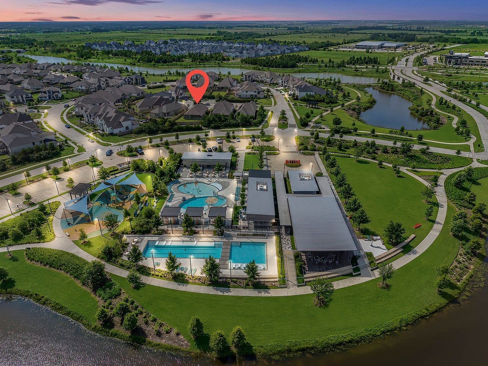 Aerial dusk view of a master-planned community with a resort pool, amenity center and lake