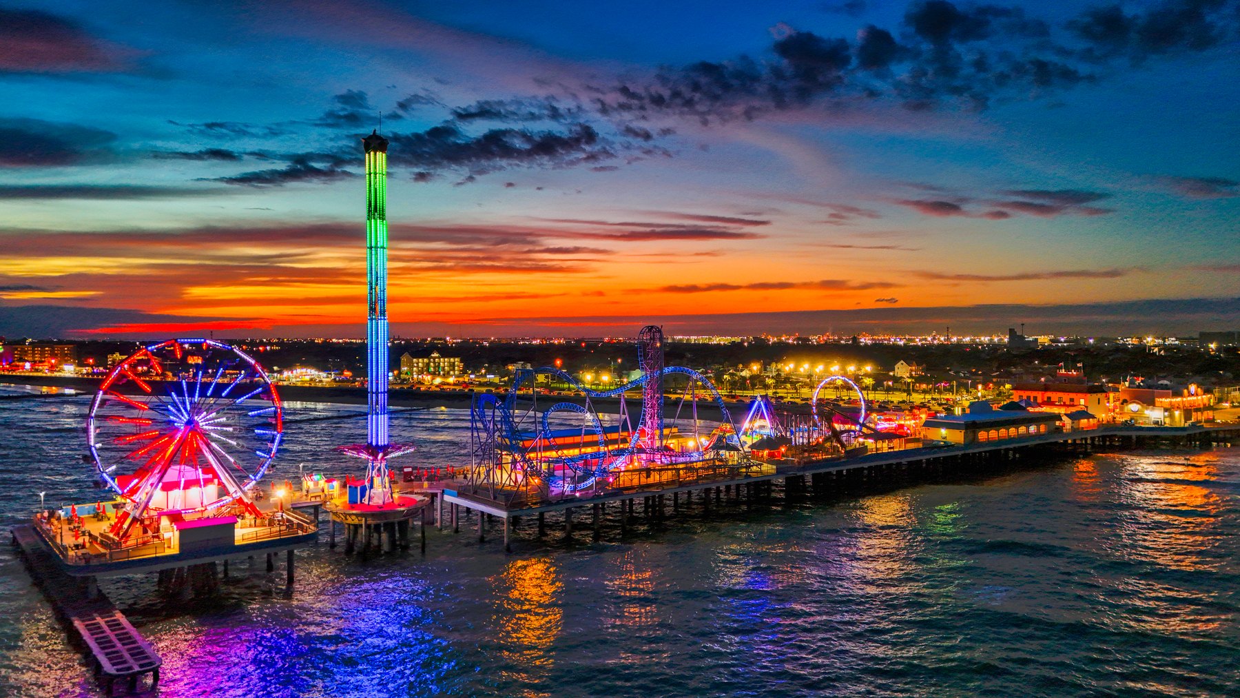 Aerial of a lit-up pier and amusement park at sunset