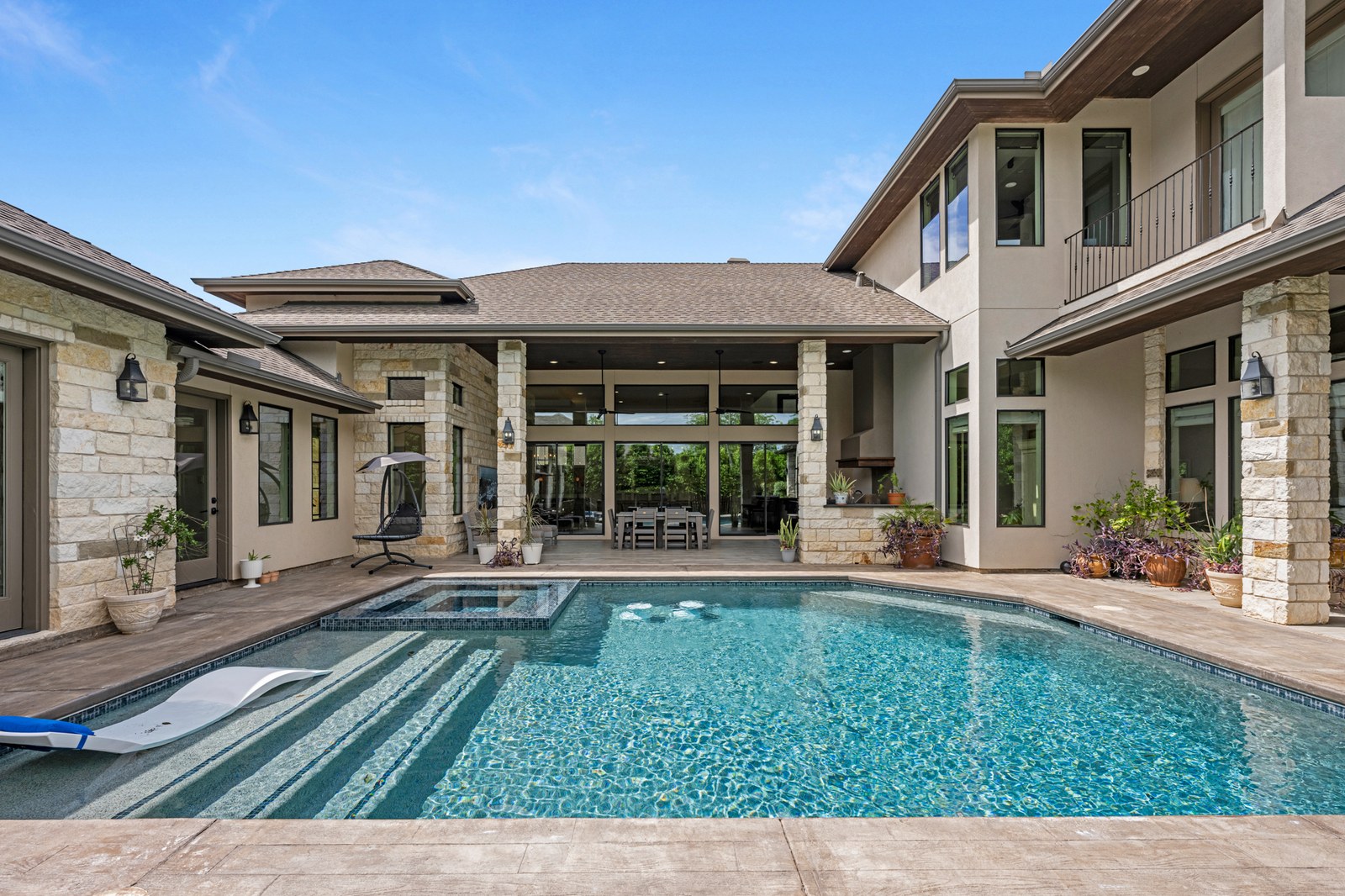 Modern stone and stucco home with a long backyard pool and tanning ledge