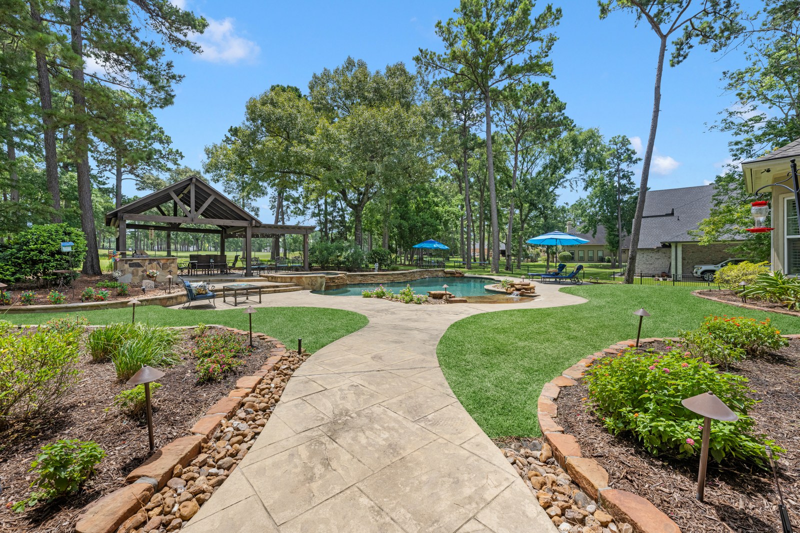 Landscaped path through tall pines to a pavilion and pool