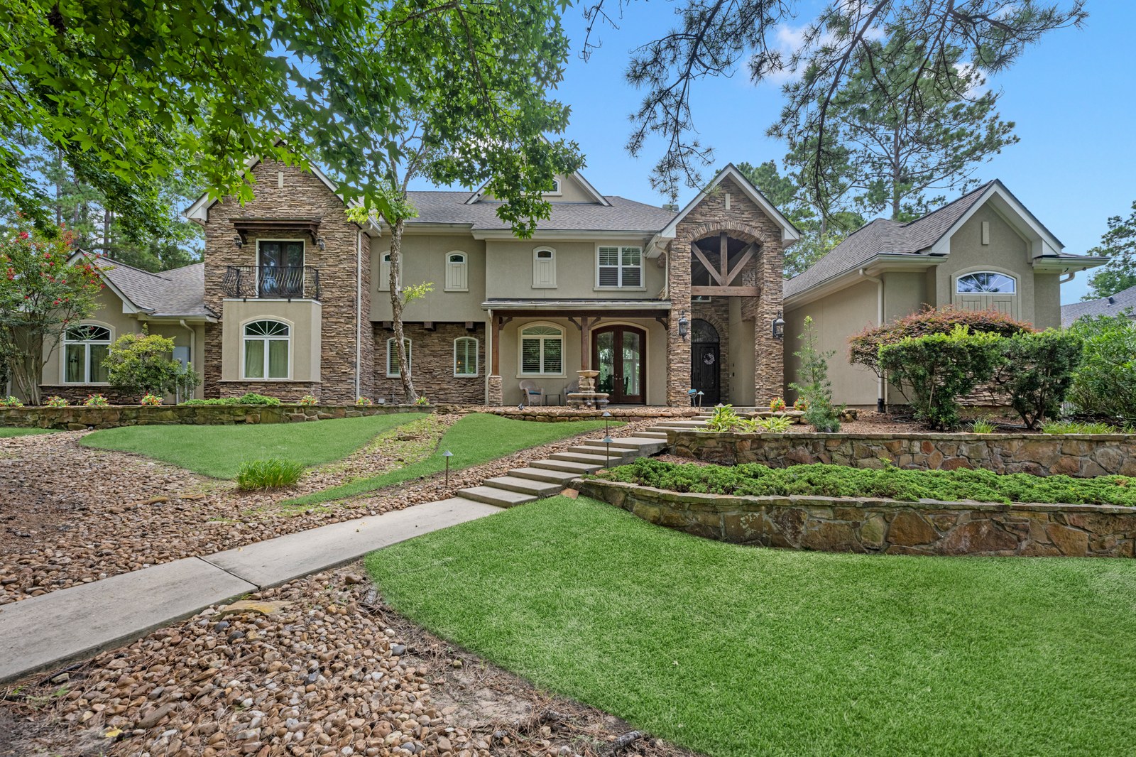 Stone and stucco two-story home with terraced stone beds and a walkway up a landscaped lawn