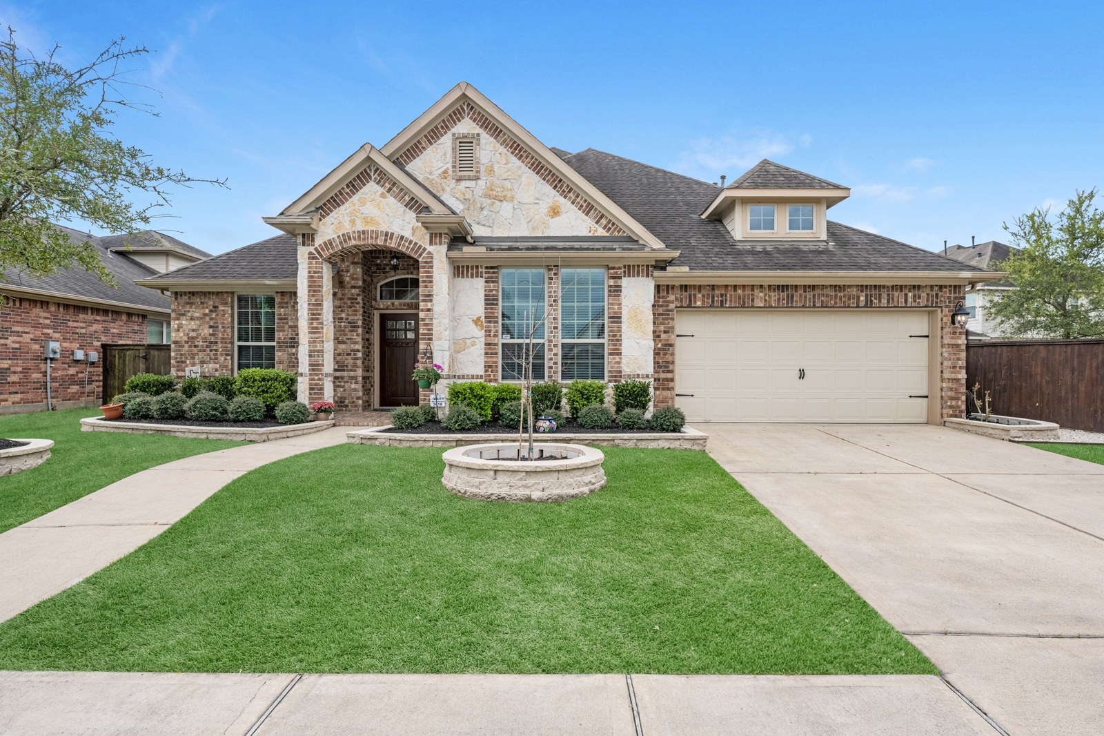 Stone and brick one-story home with an arched entry, a round stone planter and a curved front walk