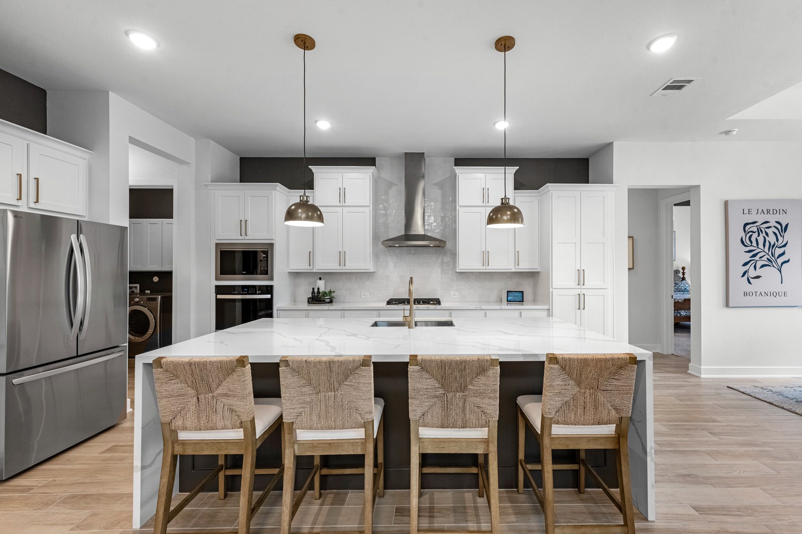 White kitchen with a marble island, woven bar stools and brass pendants