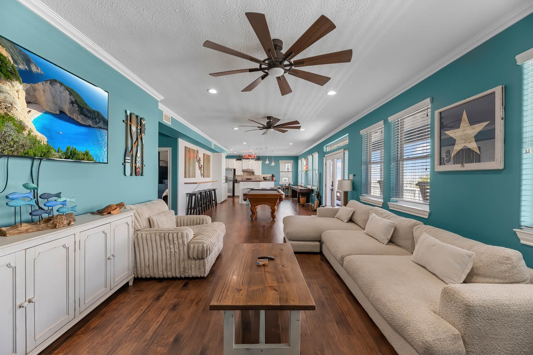 Long teal living room with ceiling fans, wood floors and a game table