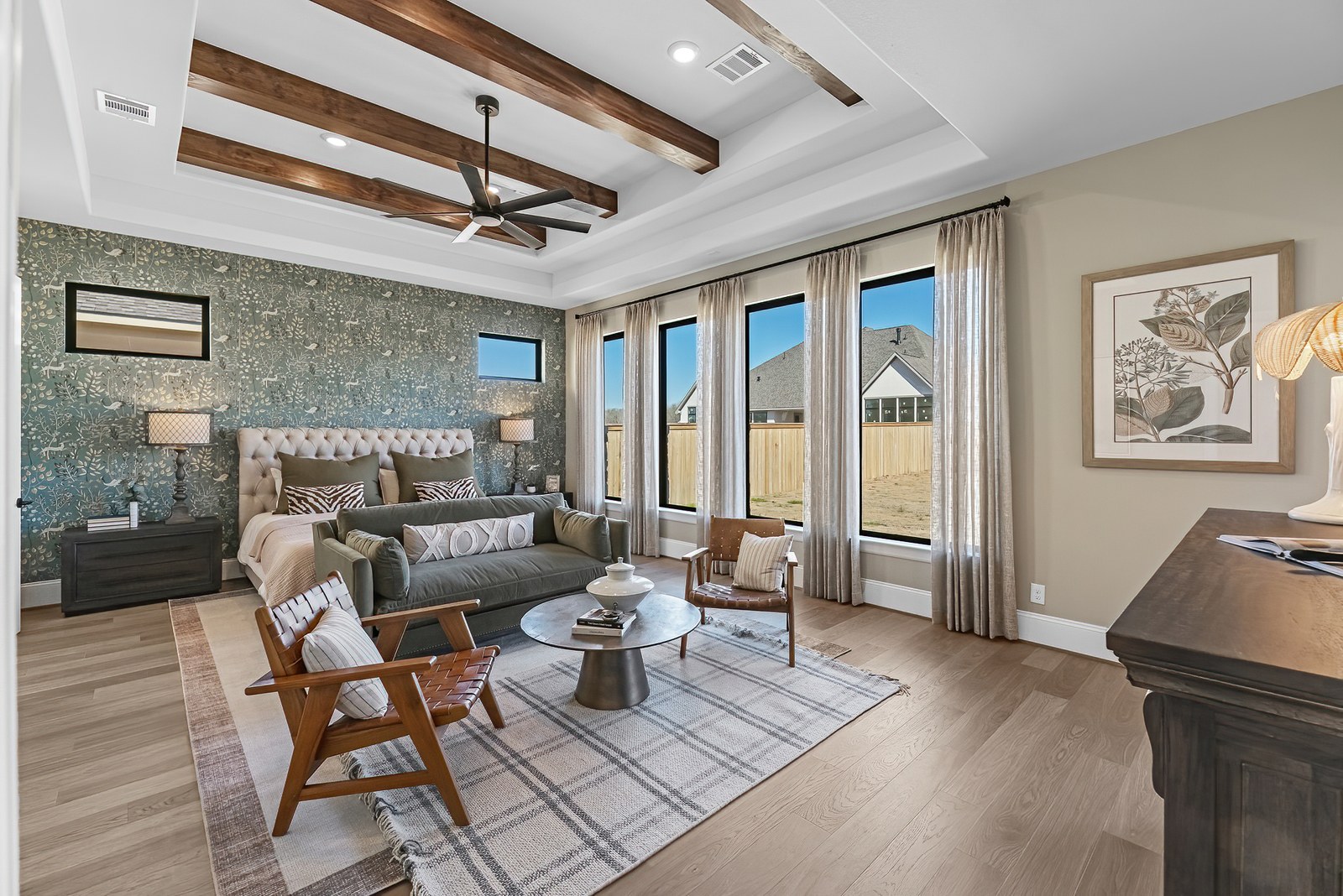 Primary bedroom with wood ceiling beams, a patterned accent wall and a sitting area