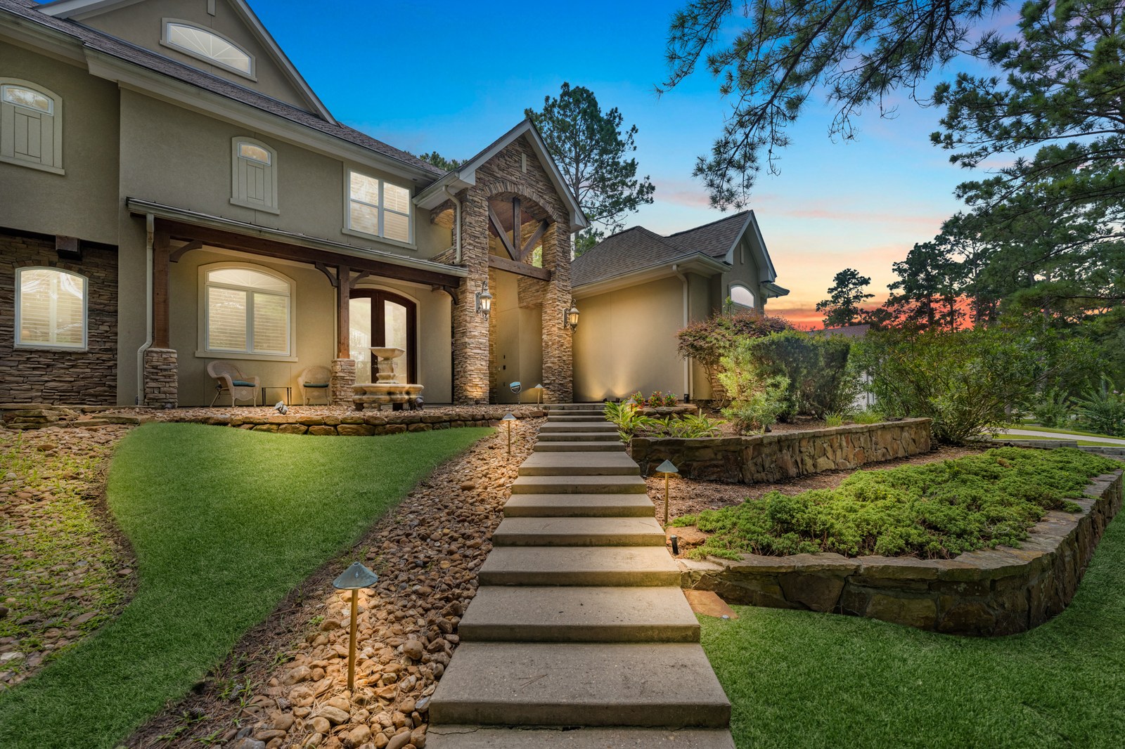 Virtual twilight of a stone and stucco home with lit path lights and stone steps under a sunset sky