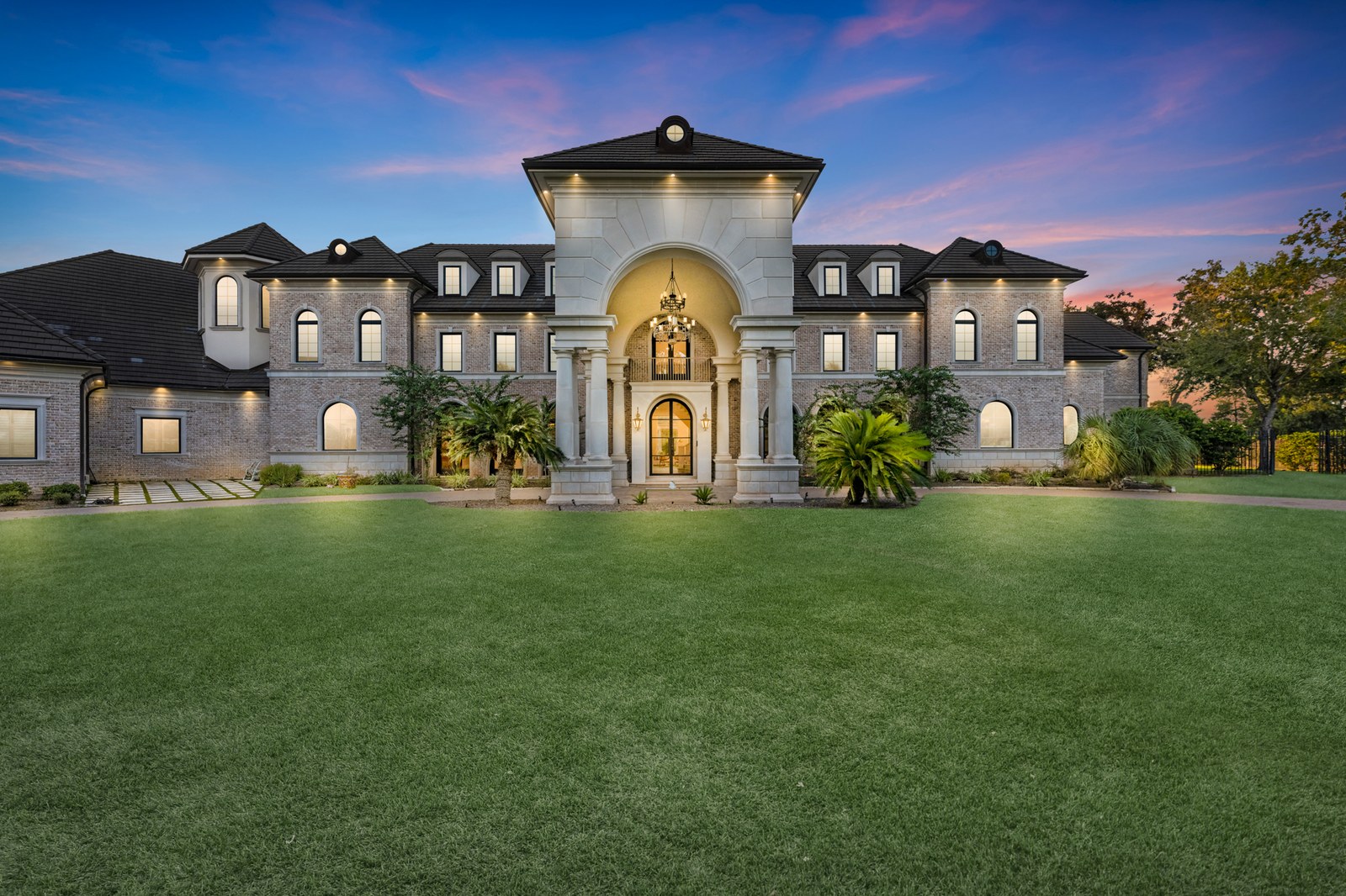 Virtual twilight of a brick estate with a columned arched entry and wide front lawn